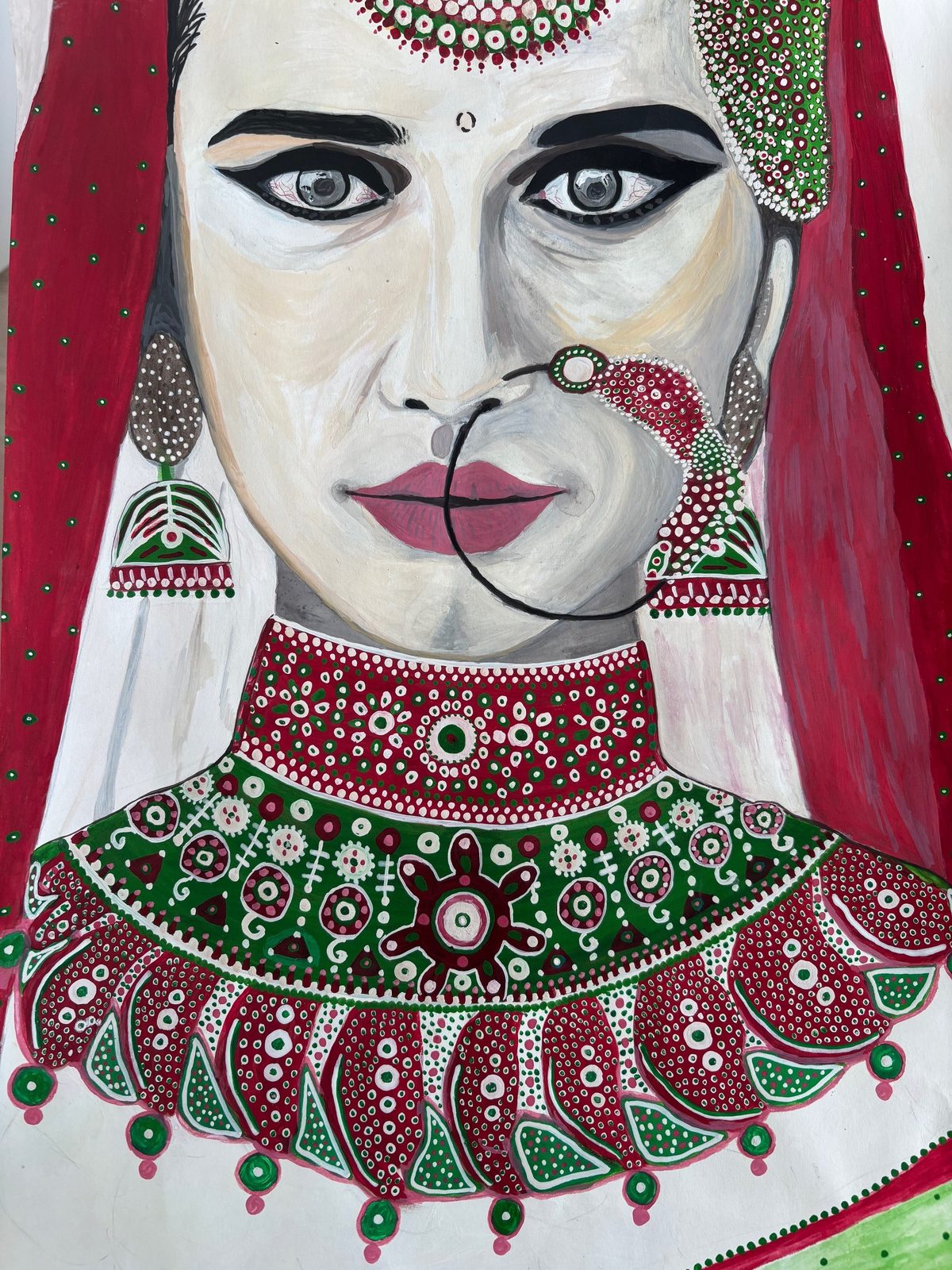 Portrait of a bride in a red veil wearing intricately dotted red, green and white traditional jewellery